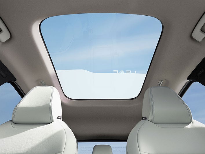 A wide-angle interior shot of a car, looking up through a large panoramic sunroof at a blue sky.